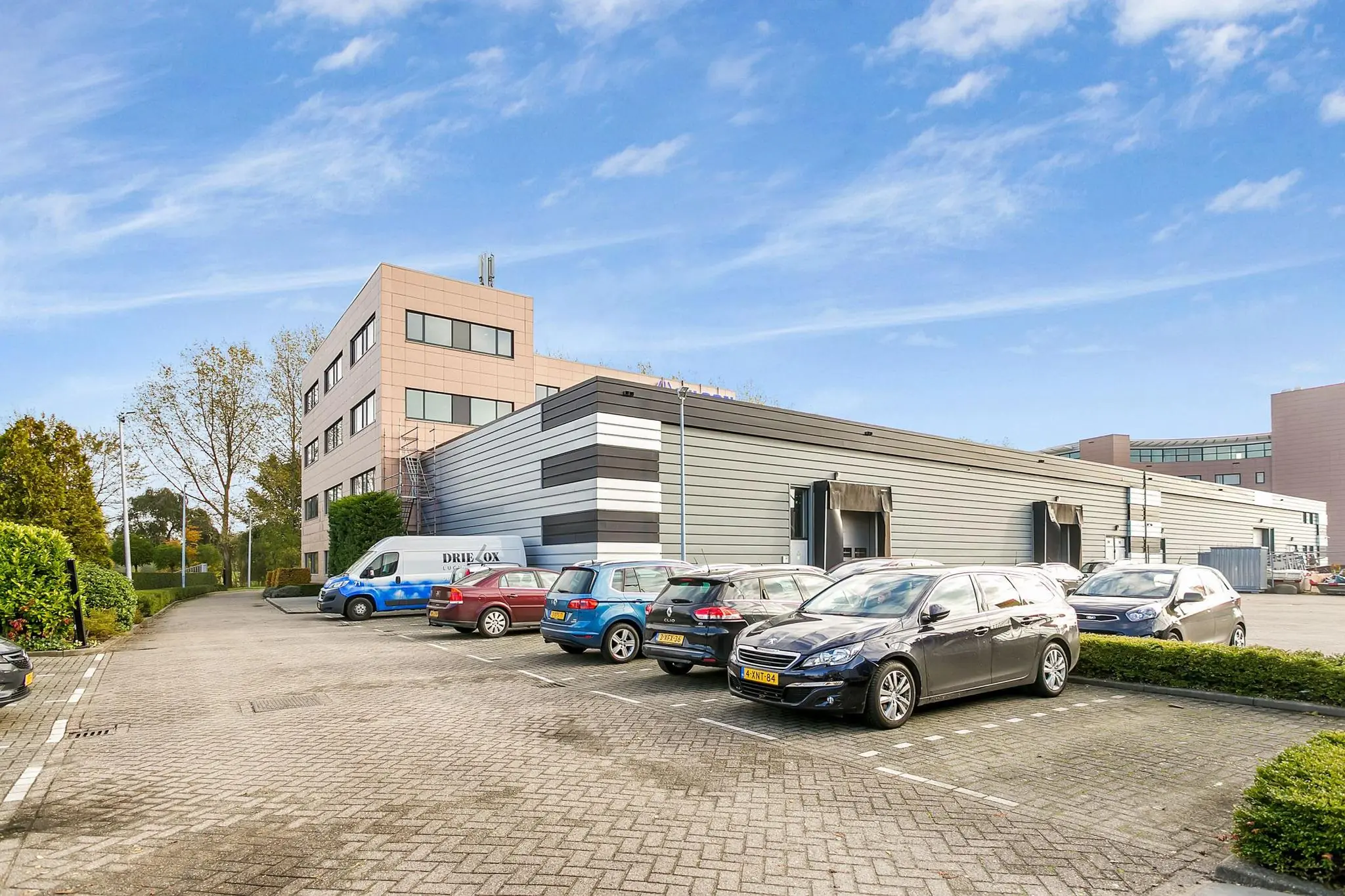 Bedrijventerrein aan de Laan van ‘s-Gravenmade met een modern kantoorgebouw, bedrijfsruimte en geparkeerde auto's.